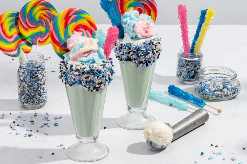 Colorful and whimsical cotton candy flavored milkshakes with rainbow lolipops and rock candy sticking out.