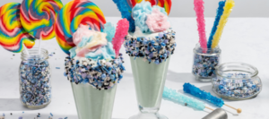 A galaxy cotton candy milkshake in two crystal glass with colorful candy and sprinkles.
