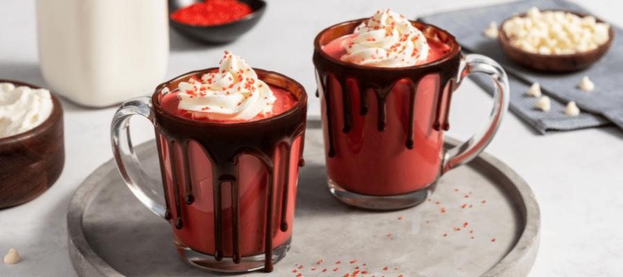 Two glass mugs with hot chocolate and decorated with chocolate sauce, whipped cream, and sprinkles.