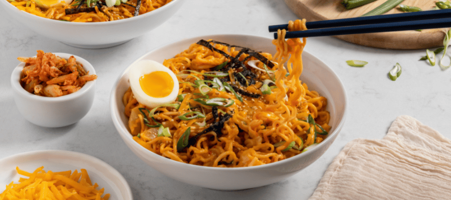 A white bowl with kimchi ramen with cheese, garnished with green onions and a soft-boiled egg.