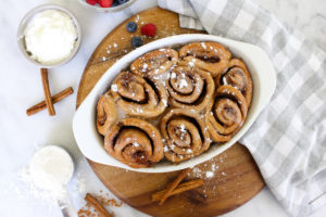 Cinnamon rolls in a baking dish adorned with berries and cinnamon sticks.