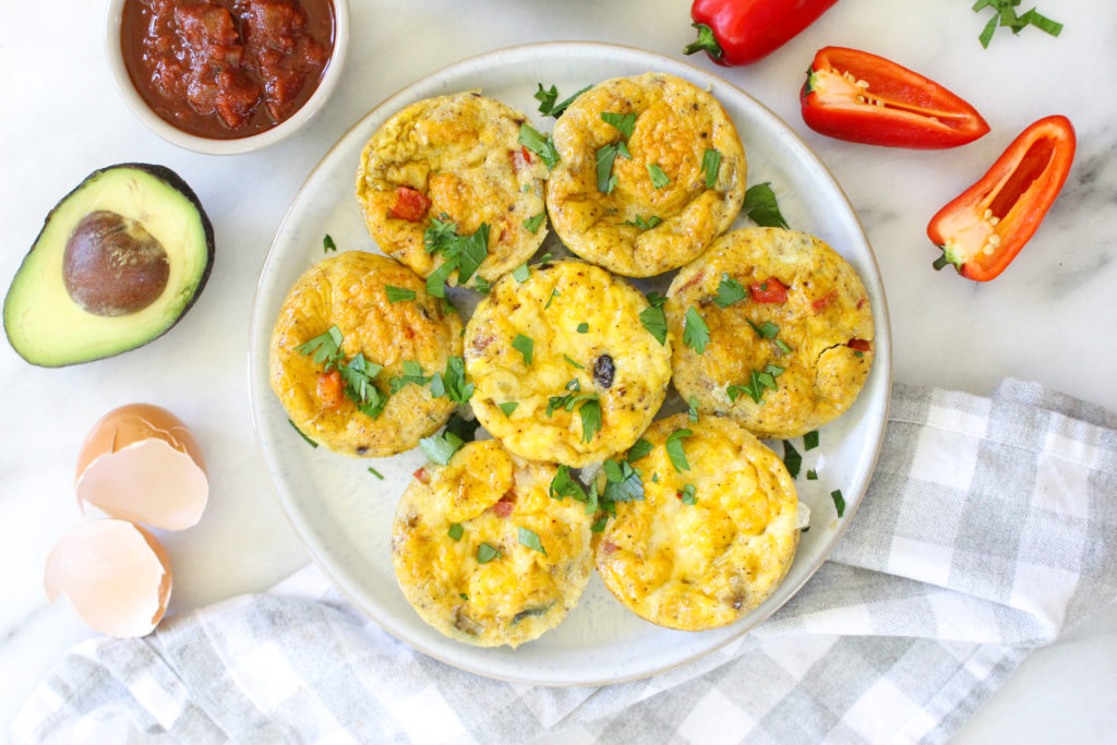 A white plate filled with flavorful tex-mex egg cups, accompanied by peppers, beans, and avocado in the background.