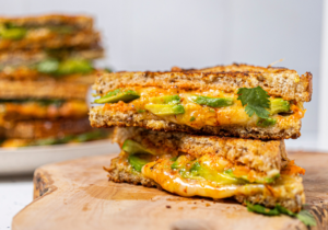 One roasted red pepper avocado grilled cheese sandwich cut in half on a wooden table.