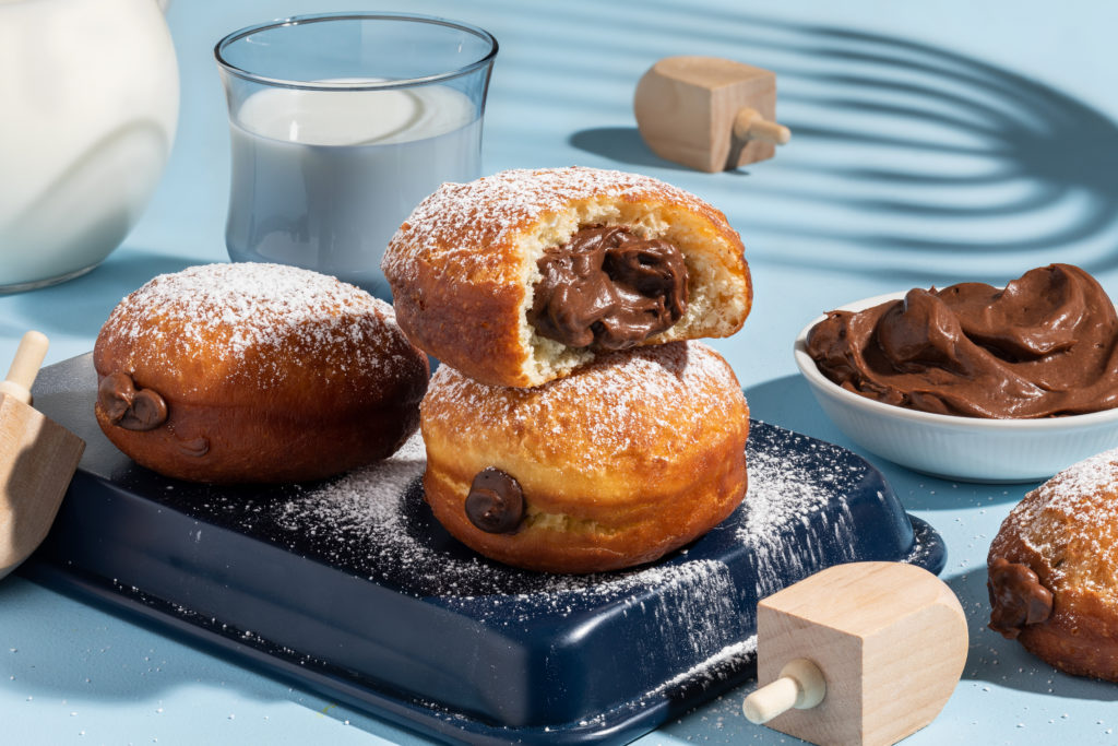 A plate with 3 donuts and a glass of milk, featuring delicious chocolate custard sufganiyot.