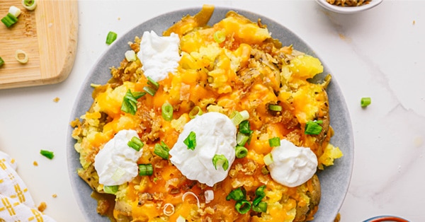 Un plato gris de nachos de papa con queso cheddar decorados con crema agria y cebollas verdes.