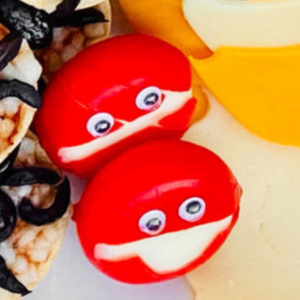 Mini cheese wheels decorated to look like silly monsters with small googly eyes and a mouth carved from their red wax.
