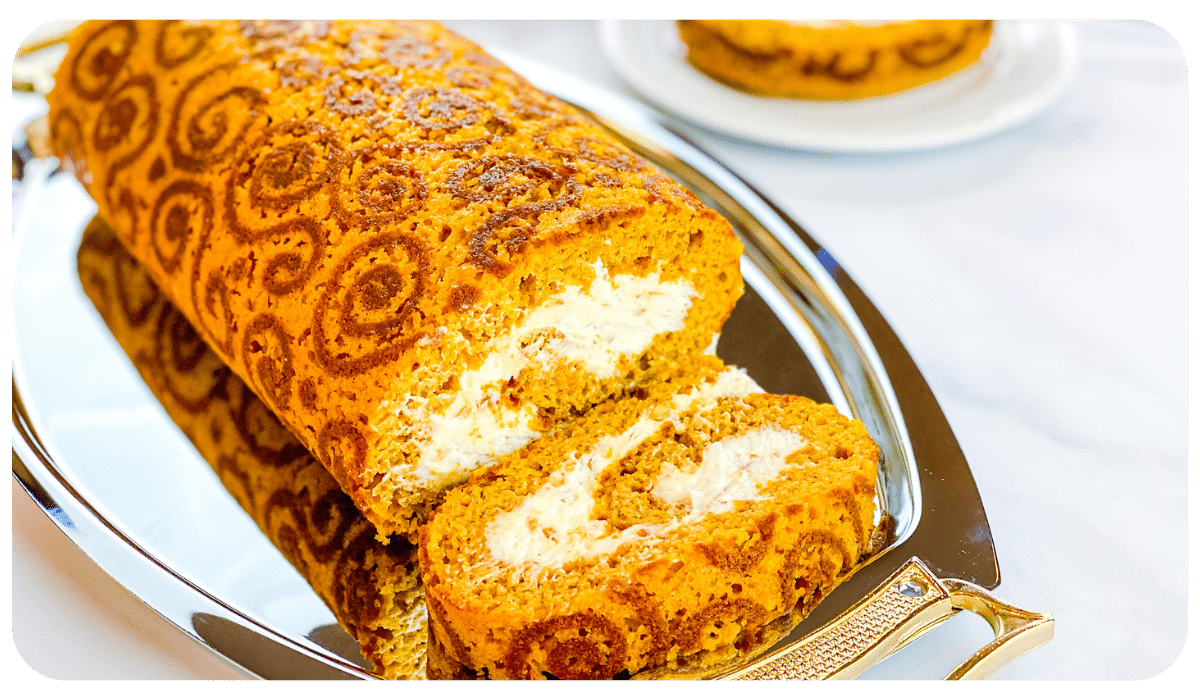 Spiced pumpkin roll decorated with swirl designs on a serving plate.