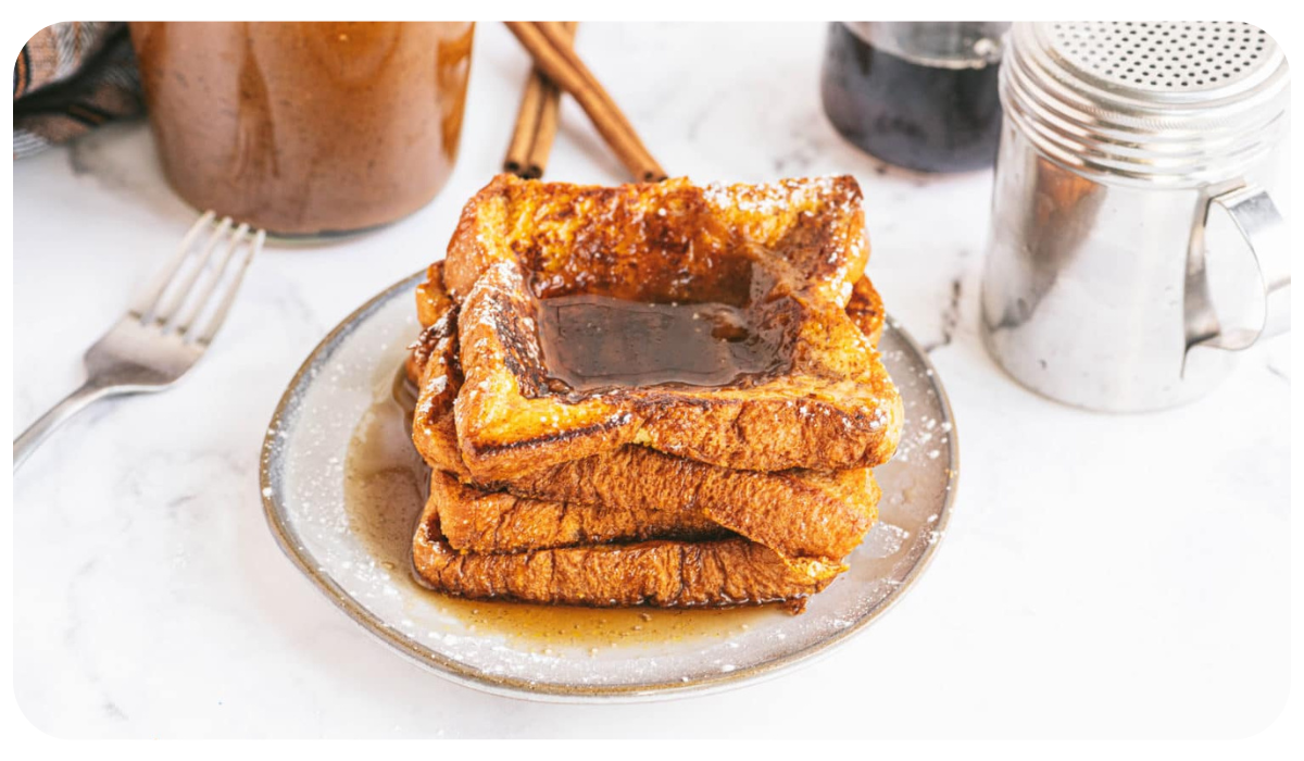 A plate of pumpkin French toast decorated with a drizzle of maple syrup and powdered sugar next to a fork.