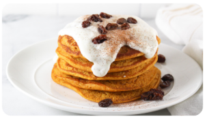 A delicious stack of pumpkin pancakes topped with yogurt frosting and garnished with raisins.