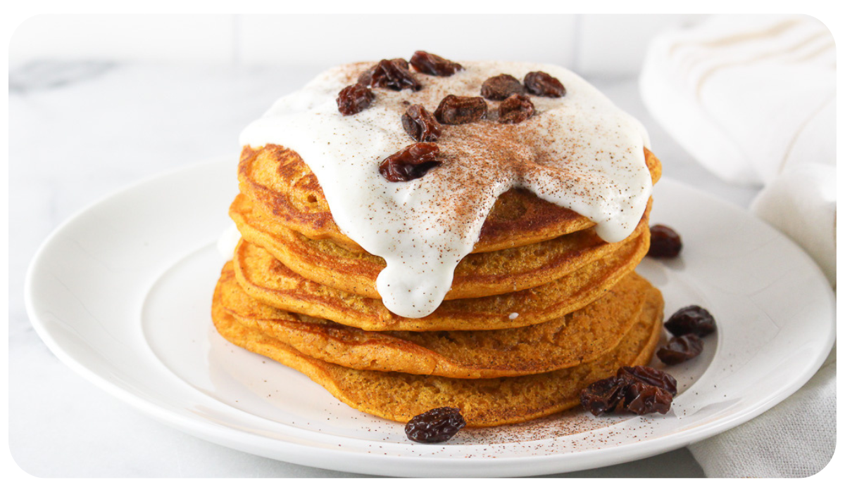A delicious stack of pumpkin pancakes topped with yogurt frosting and garnished with raisins.