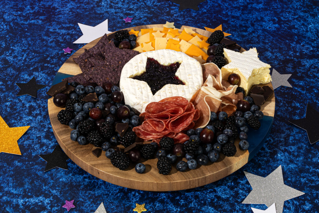 A colorful charcuterie board with meats, cheeses, and fruit. The centerpiece is brie with a star cut out.