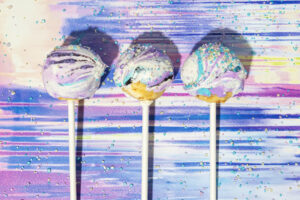 La imagen muestra 3 Cake Pops de Galaxia sobre un fondo de colores