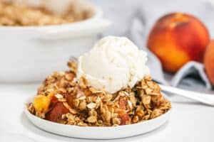 Un postre crujiente de durazno cubierto con avena y una bola de helado de vainilla.