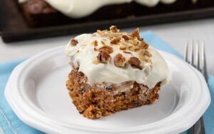 Un trozo de pastel de zanahoria cubierto con nueces servido en un plato.