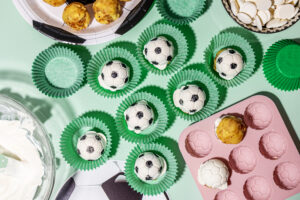 Soccer-ball style cake pops in green paper liners on a pastel green surface.